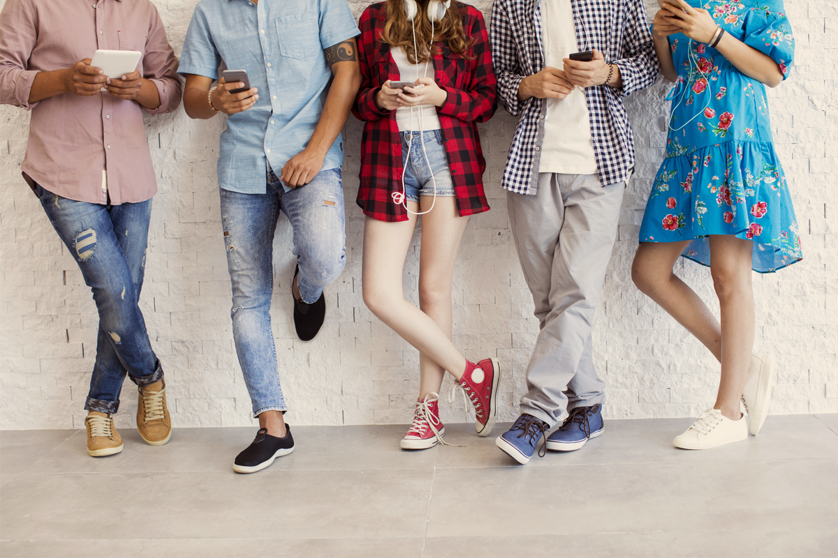 Des jeunes accotés sur un mur qui regardent leur téléphone.