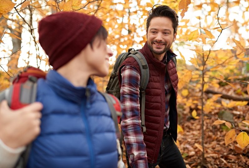 Portait of an attractive millennial couple walking in autumn nature with backpacks and trekking on a path surrounded by orange leaves